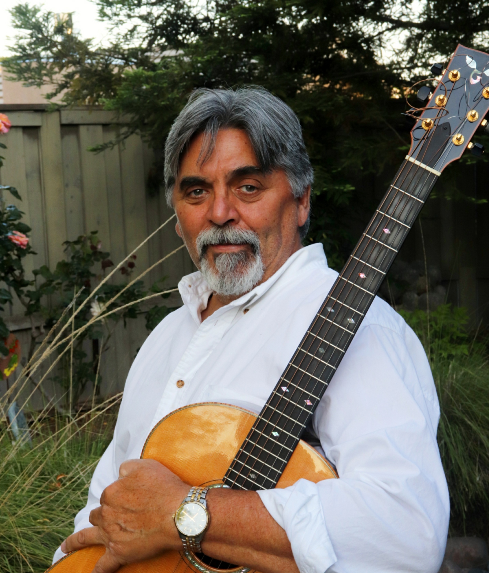 Mark in white shirt and holding guitar in garden area